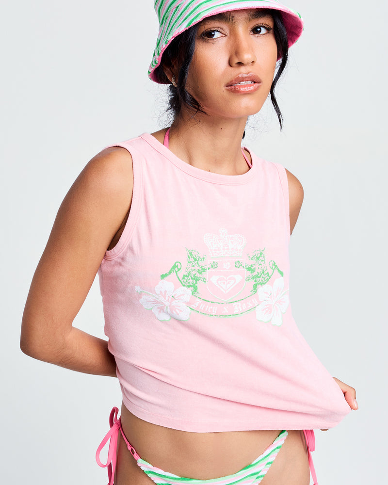 A woman wears a Candy Pink Roxy x Juicy Crest Tank Top, pink and green striped bikini bottoms, and a matching bucket hat, standing against a plain light background.