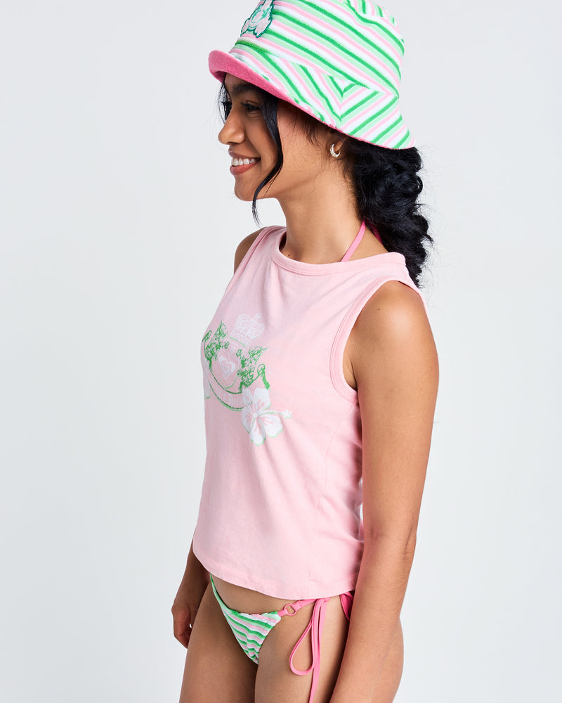 A woman in the Roxy x Juicy Crest Tank Top, pink and green striped bikini bottoms, and a matching bucket hat stands sideways and smiles against a plain light background.
