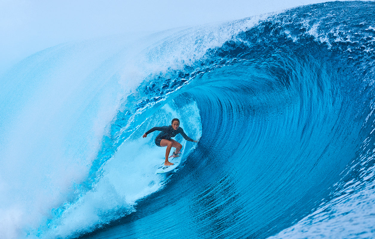 Surfer riding a large wave in clear blue water